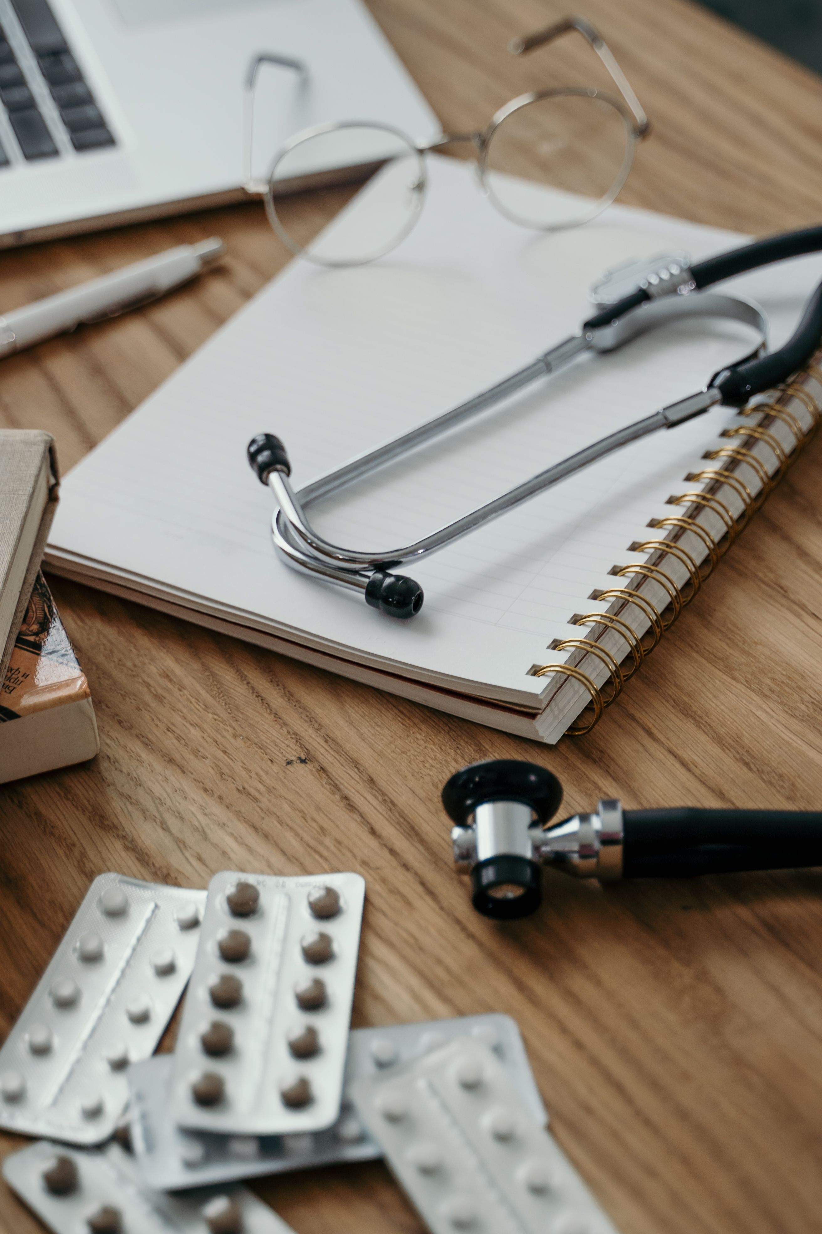 A stethoscope, notepad, glasses and medications on a desk